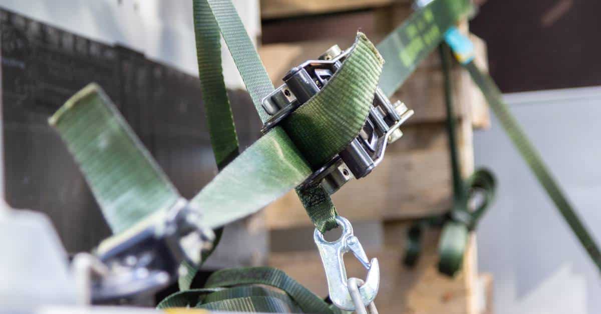 A green tie-down strap is fastened to an anchor point on a flatbed truck for transporting goods.