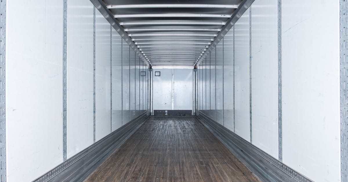 The inside of an empty semi-trailer with white walls, vertical metal lines, and scuffed hardwood flooring.
