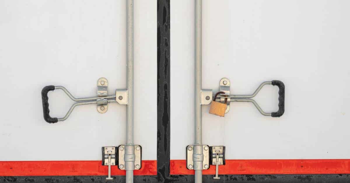 A close-up image of the back door of a white cargo freight truck that is secured by silver bars and handles.