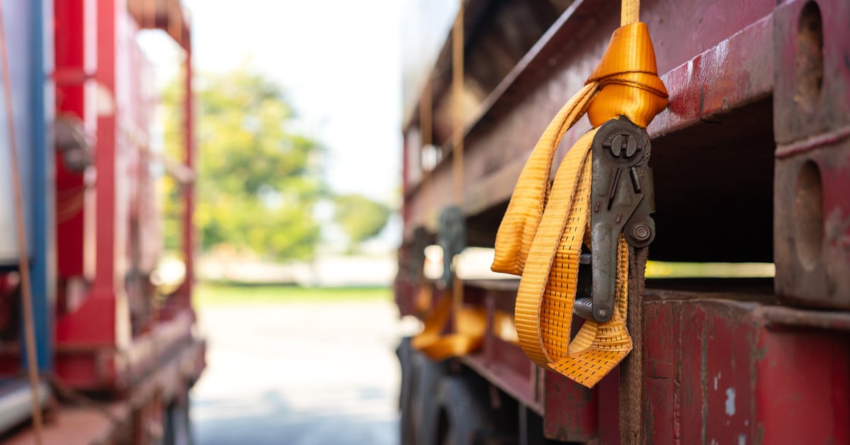 A close up of a rusty load locking ratchet strap latch. The straps are yellow in color and secured by the latch.