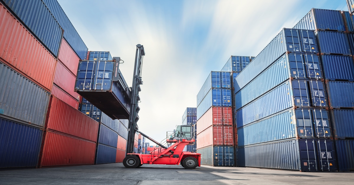 A red forklift raises a blue intermodal shipping container onto another container on a shipping container ship.