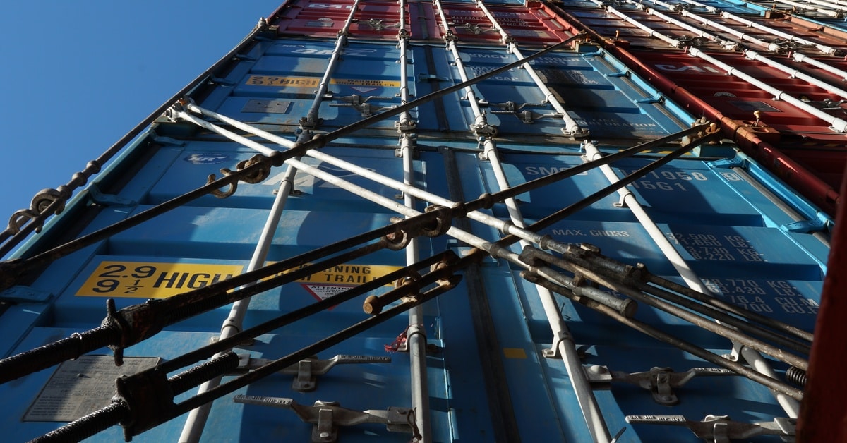 Multiple shipping containers in different colors stacked on top of each other and secured by load lock bars.