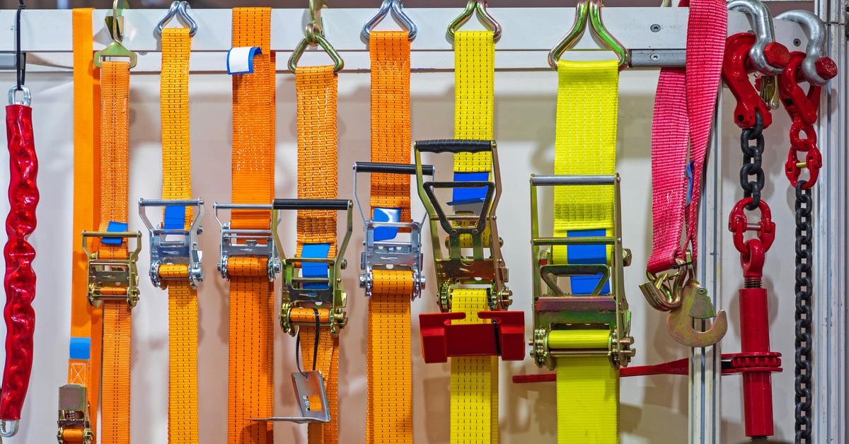 Yellow, orange, and red ratchet straps all hang on the inside wall of a freight trailer. The straps are organized by color.